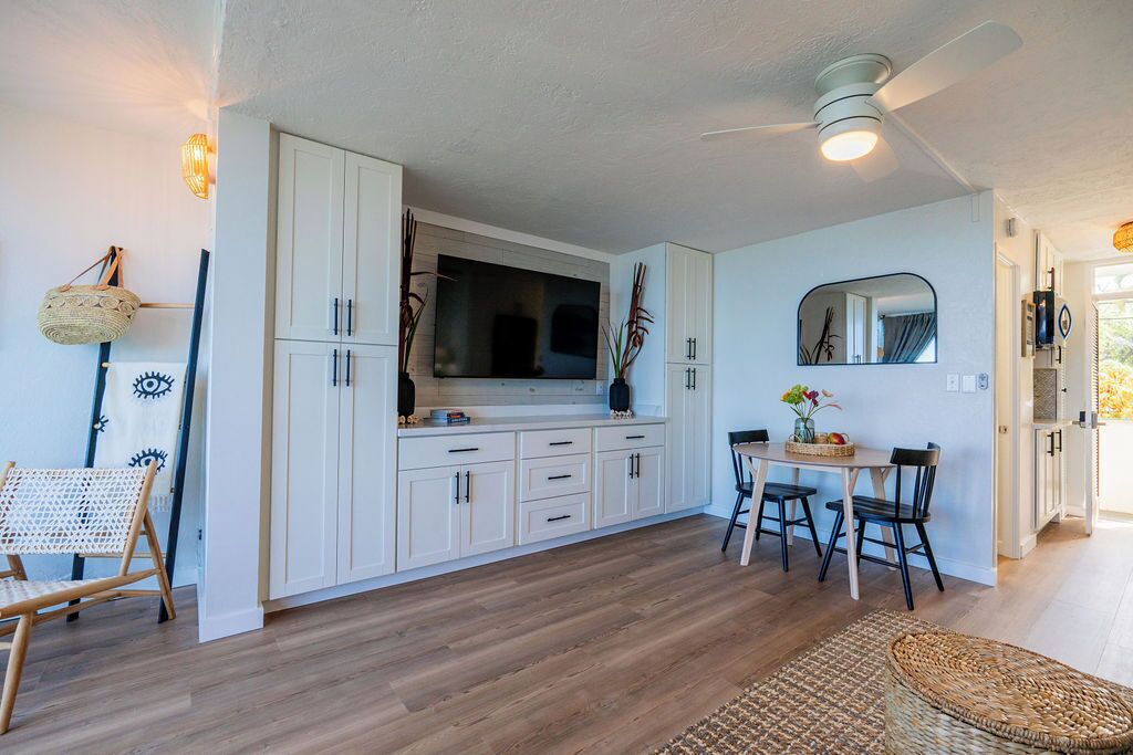 A modern kitchen with white cabinets, a dining table with chairs, and a ceiling fan.