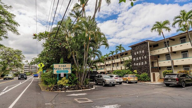A hotel named Kona Magic Sands with a signboard, parked cars, and a clear sky. - Newly Renovated Oceanfront Condo at Magic Sands Beach (Kailua-Kona)