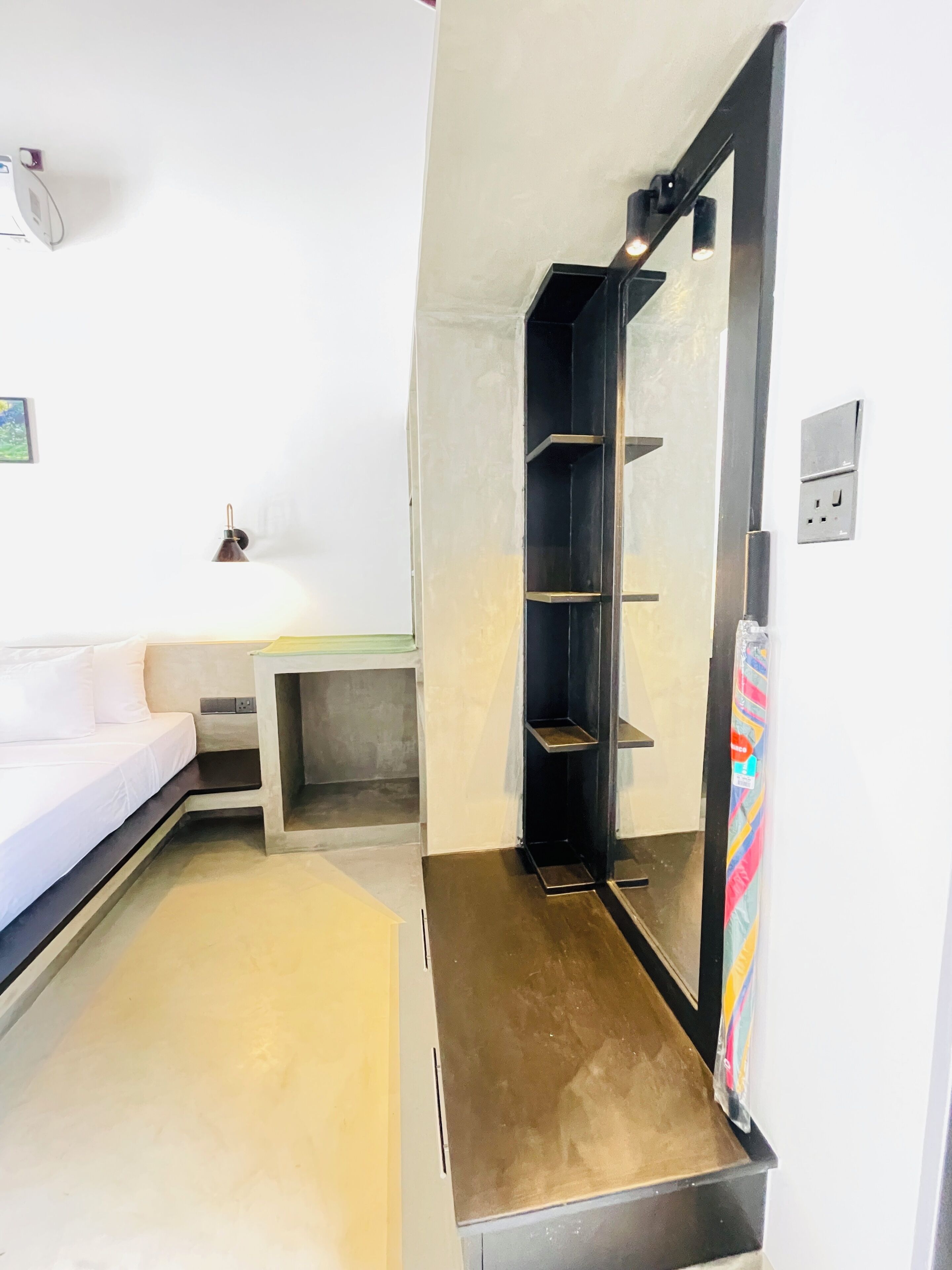 A modern bathroom with a shower, a toilet, and a sink. There is a white wall with a power outlet and a light switch.