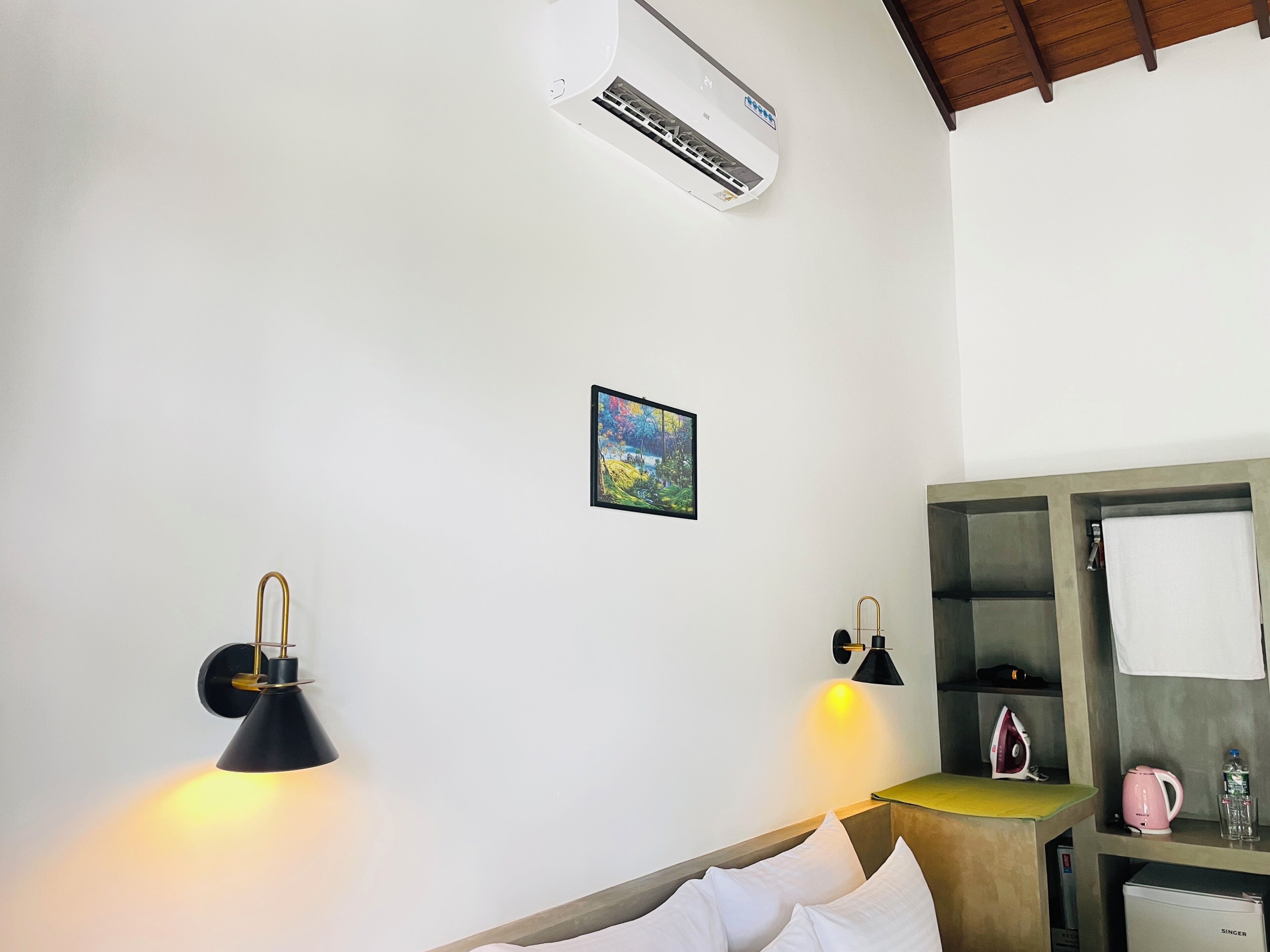 A hotel room with a bed, bedside lamps, a small painting, a mirror, and a kitchenette.