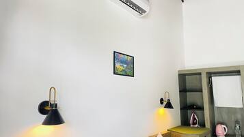 A hotel room with a bed, bedside lamps, a small painting, a mirror, and a kitchenette.