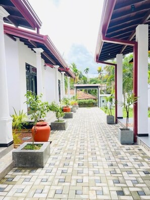 A covered walkway with potted plants and a tiled floor, leading to a building with a red roof. - Thara Inn Villa (Dikwella)