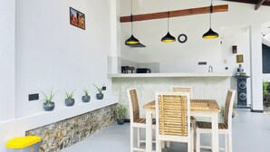 Comedor con mesa y sillas de madera, pared de piedra y lámparas colgantes.