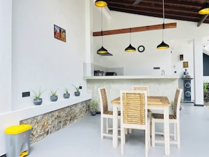 A dining area with a wooden table and chairs, a stone wall, and hanging pendant lights. - Thara Inn Villa (Dikwella)