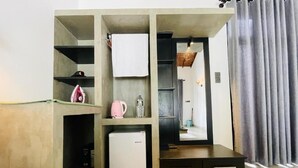 Una habitación compacta con kitchenette, un refrigerador pequeño, un espejo y una cortina.