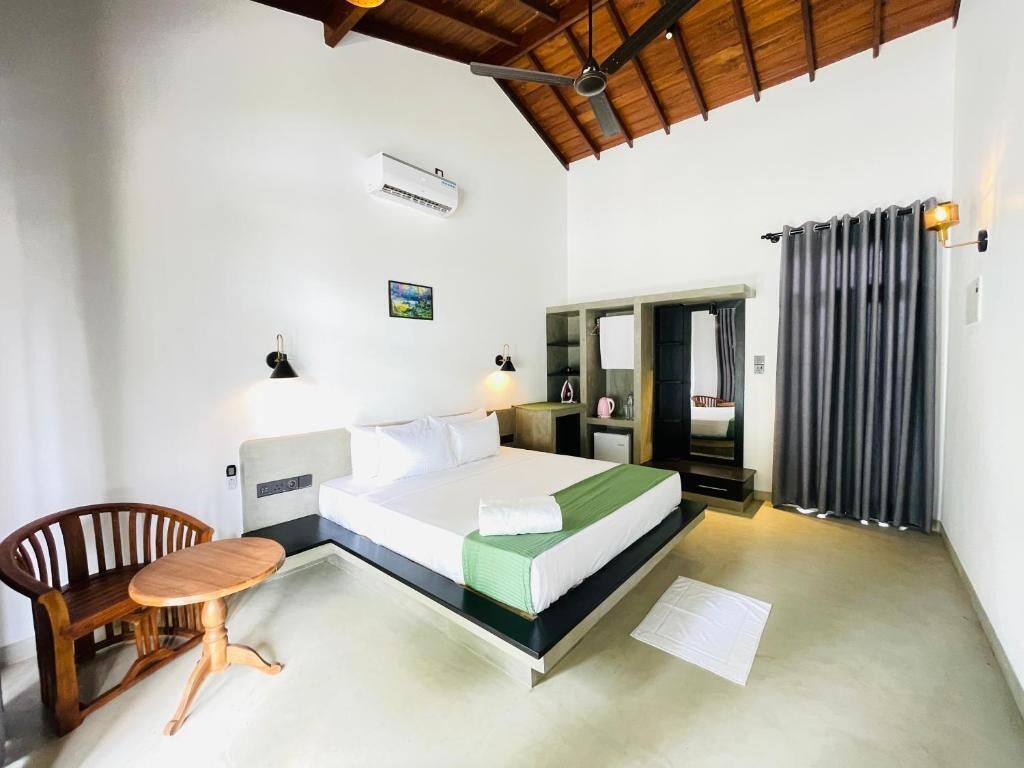 Un dormitorio con una cama, una silla, una mesita, un espejo y una ventana con cortinas.