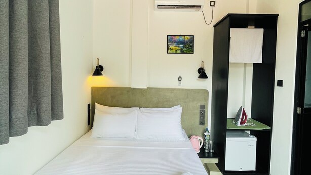 Una habitación de hotel con cama, mesita de noche, equipo de aire acondicionado y una pequeña kitchenette.