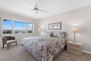 A bedroom with a large bed, a chair, a nightstand, a lamp, and a ceiling fan. - ☀️Beach Front-Sunset Views | Pool and Easy Beach Access | Sand Caper #702 🌴 (Fort Myers Beach)