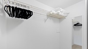 A white closet with a hanging rod and a folded shelf, a mirror, and a carpeted floor. - ☀️Beach Front-Sunset Views | Pool and Easy Beach Access | Sand Caper #702 🌴 (Fort Myers Beach)