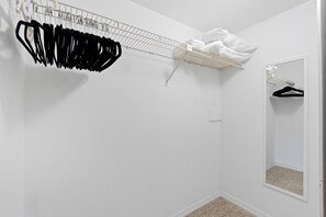 Ein weißer Kleiderschrank mit Kleiderstange und einer gefalteten Ablage, einem Spiegel und einem Teppichboden.