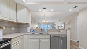 A modern kitchen with white cabinetry, a stainless steel dishwasher, and a view to the outside. - ☀️Beach Front-Sunset Views | Pool and Easy Beach Access | Sand Caper #702 🌴 (Fort Myers Beach)