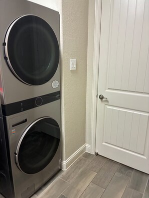 A stacked washer and dryer unit in a corner with a white door and a textured wall. - Your Sleep Destination Awaits (Cypress)