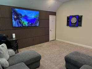 Ein Zimmer mit an der Wand befestigtem Fernseher, einer Dartscheibe und zwei Hocker.