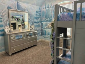 Ein Kinderzimmer mit Etagenbett, Kommode und einer Wandmalerei einer verschneiten Landschaft.