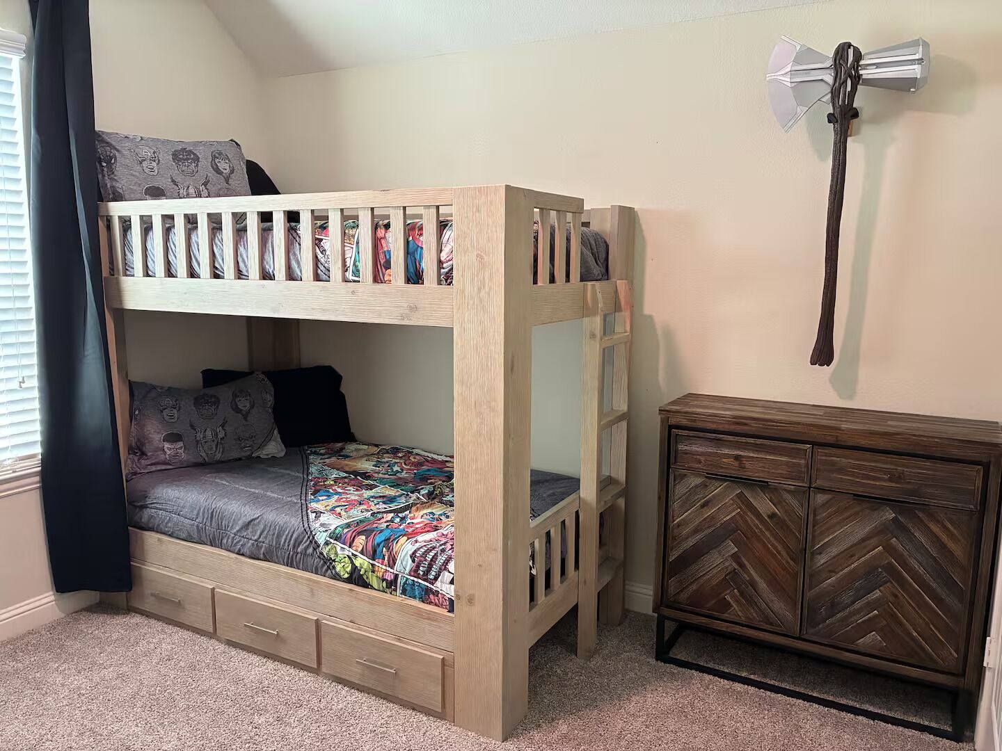 Un lit superposé avec un tiroir de rangement, une commode à motifs chevrons et un porte-manteau mural.
