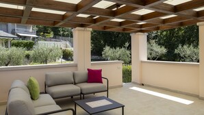 Een overdekt terras met een bank, een bijzettafeltje en een pergola.