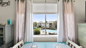 Ein Zimmer mit Blick auf einen Swimmingpool und Gebäude, ein Fenster mit Vorhängen, ein Tisch mit gemustertem Tischläufer und eine Kommode mit einem Schild.