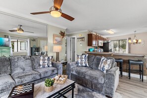 A spacious living area with a large grey sofa set, a coffee table with a chessboard, and a ceiling fan. - ⭐Walk to Beach | Crystal Village II 15B | Community Pool 🏊️ (Miramar Beach)