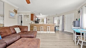 Een woonkamer met een bruine leren bank, een keuken met houten kastjes en een eettafel met witte stoelen.