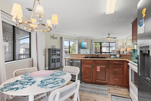 A modern kitchen with a central island, a dining area with a round table, and a view of the outdoors. - ⭐Walk to Beach | Crystal Village II 15B | Community Pool 🏊️ (Miramar Beach)