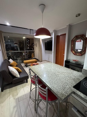 A modern kitchen with a granite countertop, red bar stools, a dining table, and a large pendant light. - A nice, comfortable, and centrally located apartment in Miraflores. (Miraflores)