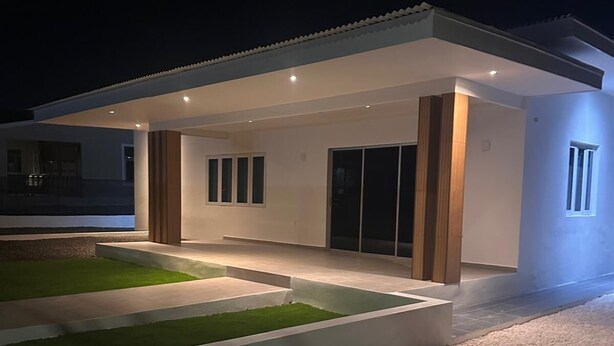 Una casa moderna amb una terrassa coberta, un jardí ben cuidat i una entrada de grava.