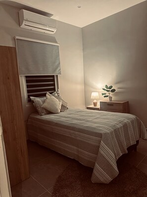 A bedroom with a bed, bedside table, lamp, and an air conditioning unit. - Modern 3BR Apartment Central Curaçao Near Beaches (Willemstad)