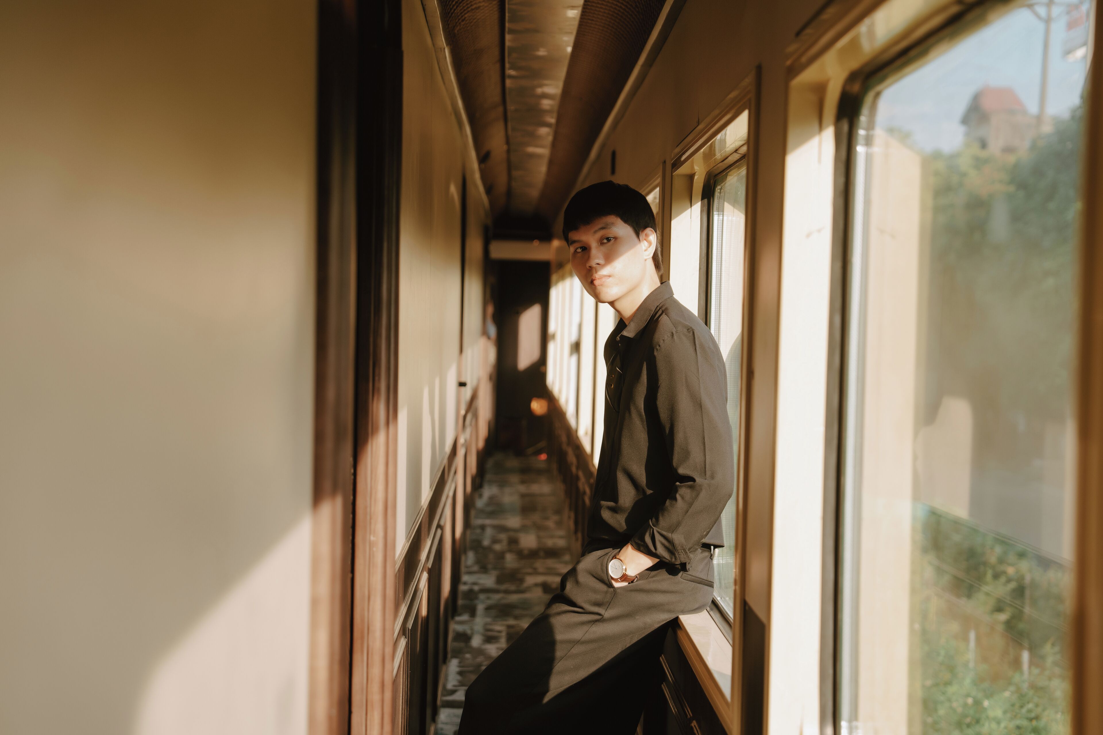 A person seated by a train window, with a view of a building and trees outside.