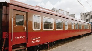 A vintage train car with 'HARACO An 11944' and 'Sjourney' text, parked on tracks with buildings in the background.