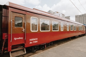 Un wagon de train ancien, portant les inscriptions « HARACO An 11944 » et « Sjourney », est garé sur des voies ferrées, avec des bâtiments en arrière-plan.