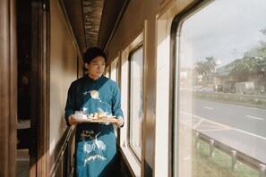 Une personne vêtue de bleu, tenant un plateau rempli de plats, se tient dans un couloir dont les fenêtres donnent sur une rue.