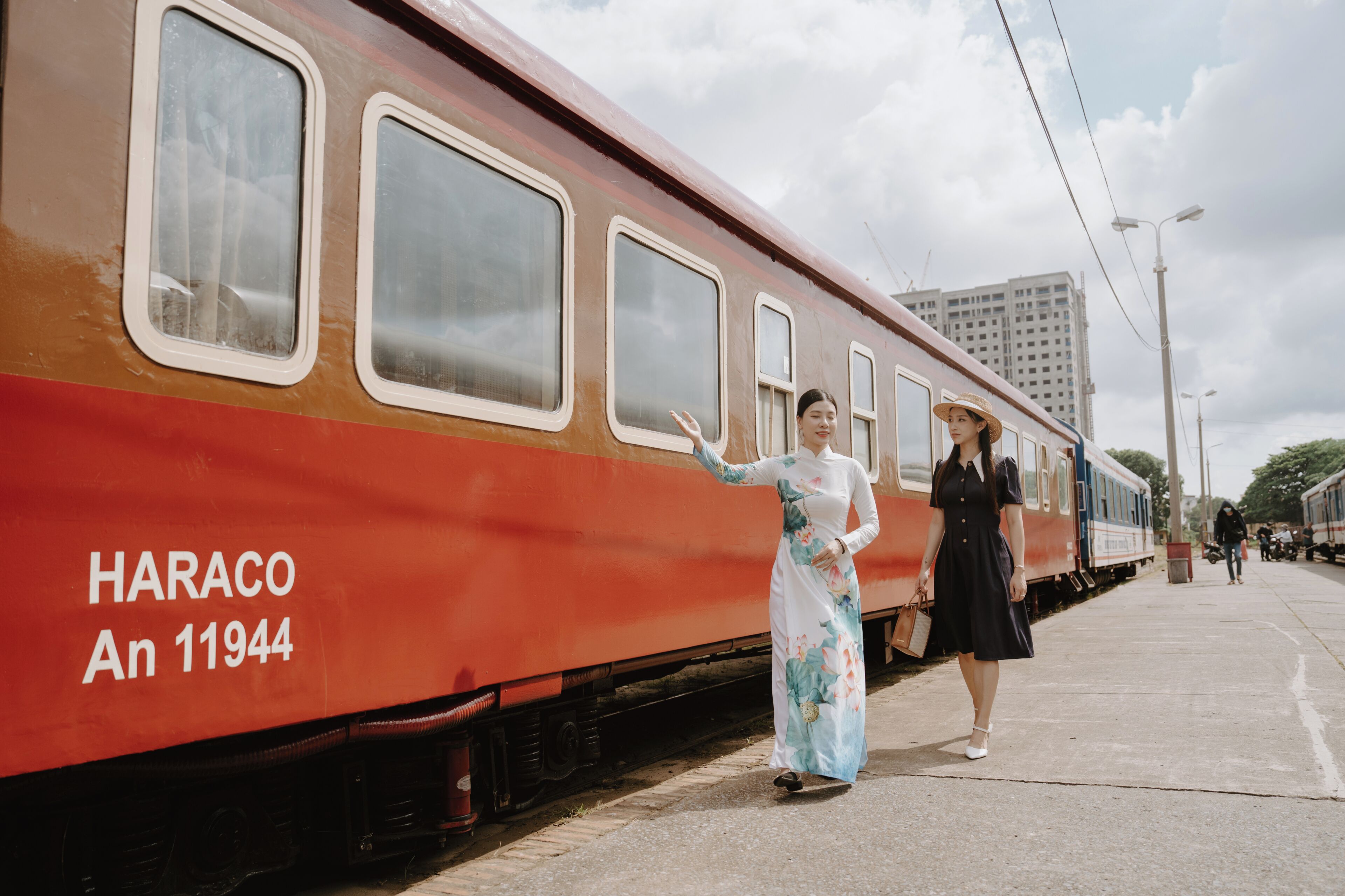 Een trein met de tekst 'HARACO An 11944' op de zijkant, een perron en een persoon in traditionele kleding.