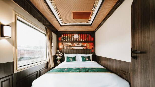 A hotel room with a large bed, a window with curtains, a decorative headboard, and a view of the outside.