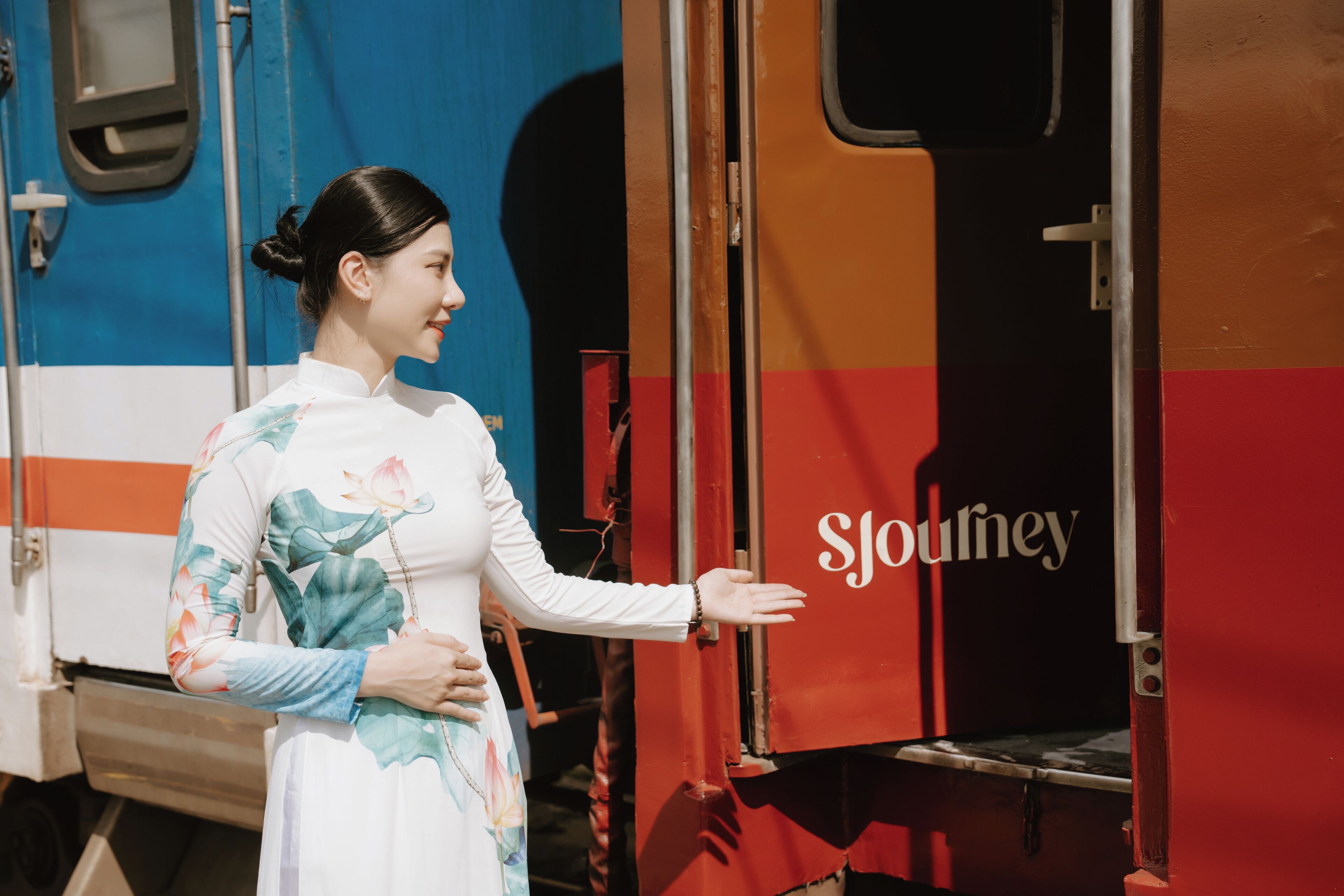 A person in a traditional dress standing next to a red and blue train with the word 'SJouney' on the side.