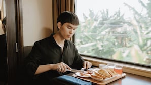 A person seated at a table with a meal, a window with a view, and a door in the background.