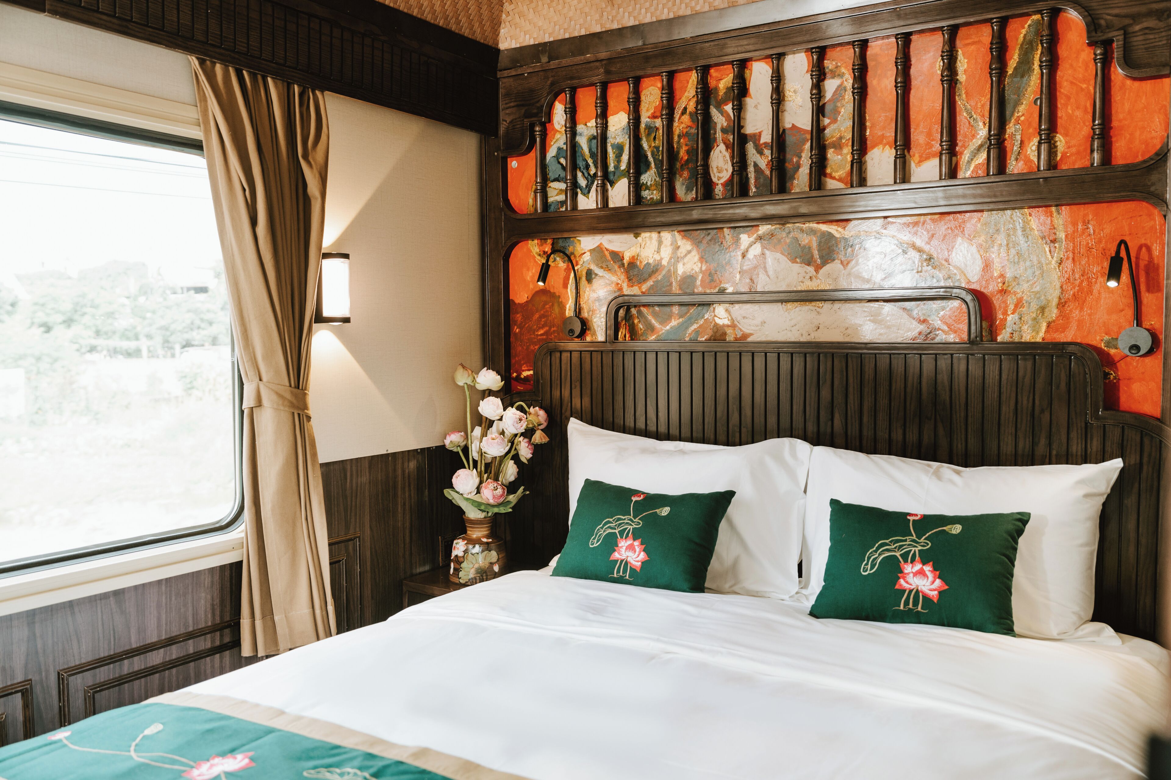 A bed with white bedding and green pillows, a vase with flowers, and a window with curtains.