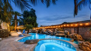 Espacio exterior con múltiples piscinas, suelo de piedra, palmeras y una cascada.