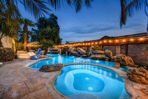 A multi-pool outdoor setting with stone flooring, palm trees, and a waterfall feature.