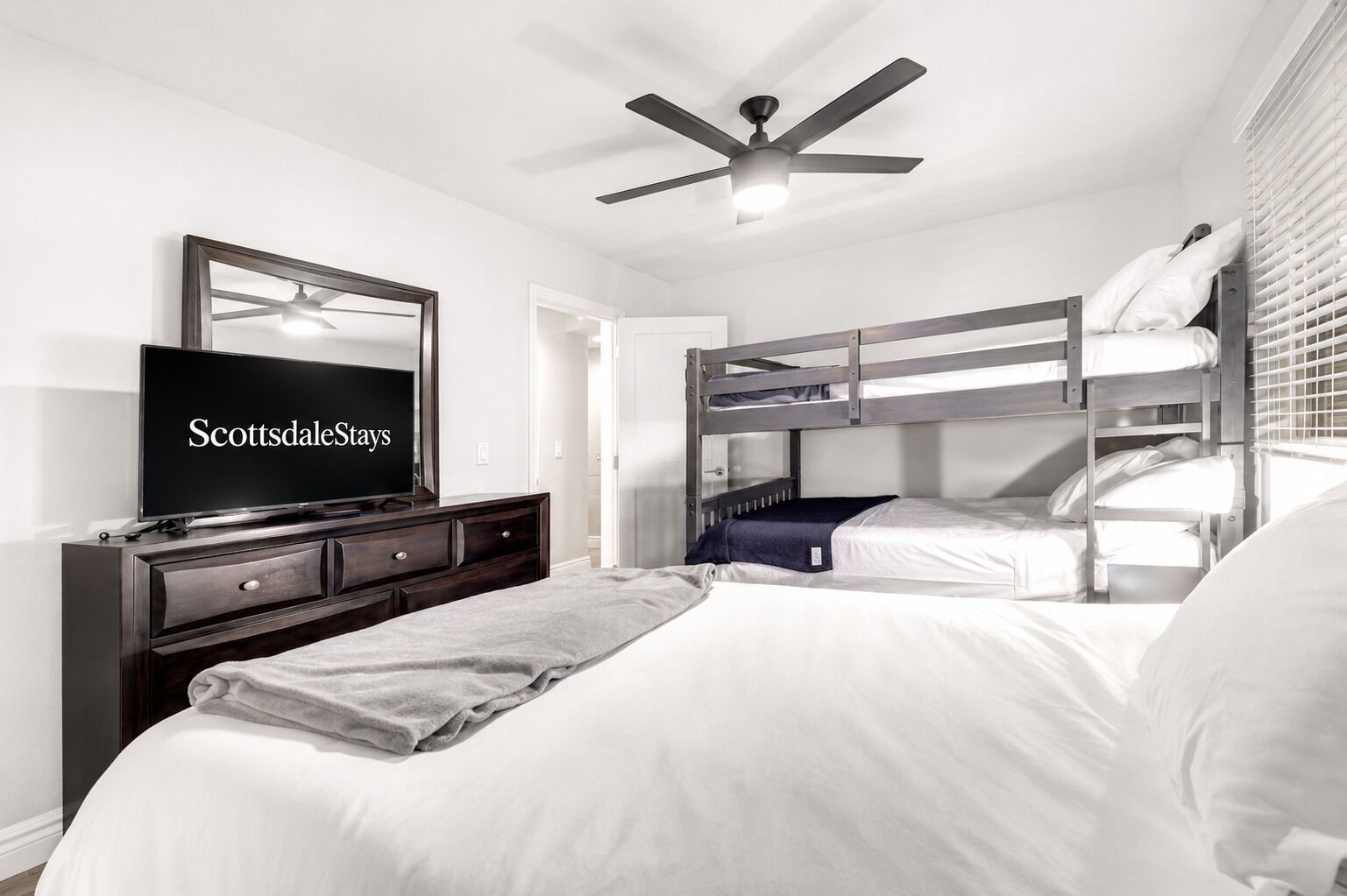 A bedroom with a bed, a TV, a ceiling fan, and bunk beds.