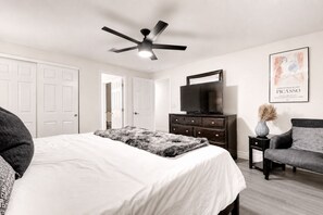 A bedroom with a bed, a dresser, a television, and a framed artwork on the wall.