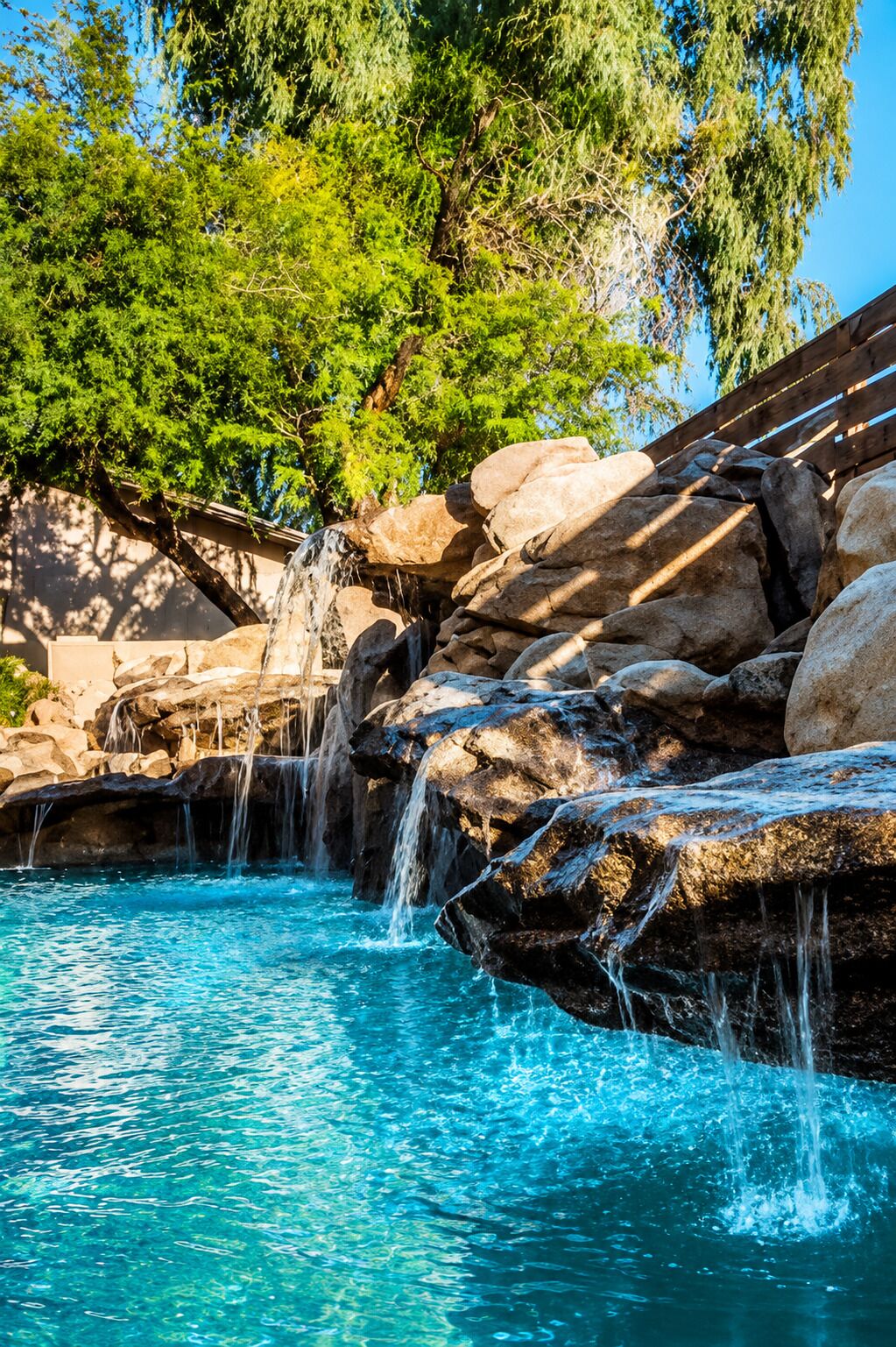A natural pool with clear blue water, surrounded by large rocks and trees.