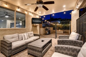 A patio area with a sofa, chairs, a TV, and a ceiling fan.