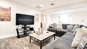 Amplia sala de estar con un televisor de pantalla plana grande, un sofá gris y una mesa de centro con objetos decorativos.