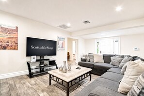 A spacious living room with a large flat-screen TV, a grey sofa, and a coffee table with decorative items.