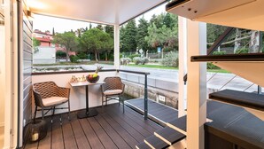 A covered outdoor seating area with two chairs and a table, overlooking a street and greenery. - Dream Holiday on the Water in Portoroz (Piran)