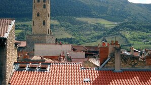 A tower with a flag, a red-tiled roof, and a mountainous background. - Hôtel du Commerce (Millau)