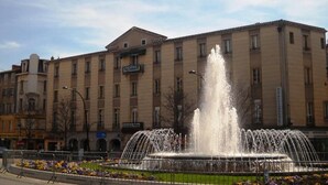A hotel with a fountain in front, surrounded by a flower bed. - Hôtel du Commerce (Millau)