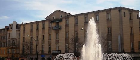 A hotel with a fountain in front, surrounded by a flower bed.