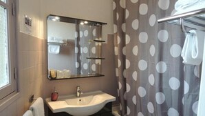 A bathroom with a white sink, a mirror, a towel rack, and a shower curtain with a polka dot pattern. - Hôtel du Commerce (Millau)