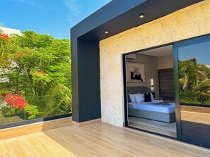 Une chambre moderne dotée d’une grande porte-fenêtre coulissante donnant sur un balcon, d’un lit avec un matelas gris et d’un climatiseur fixé au mur.